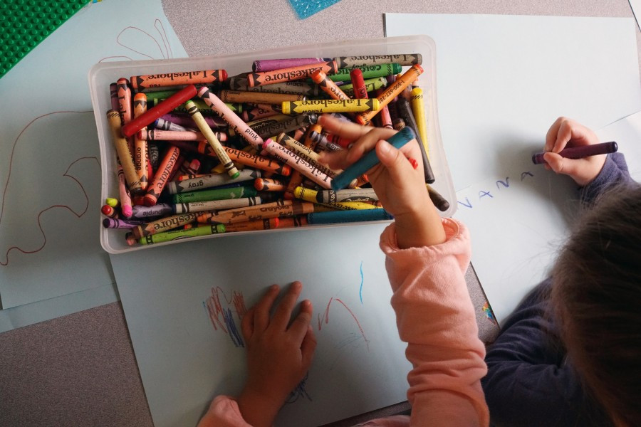 A top down shot of two kids sharing a box of crayons, drawings peeking into frame
