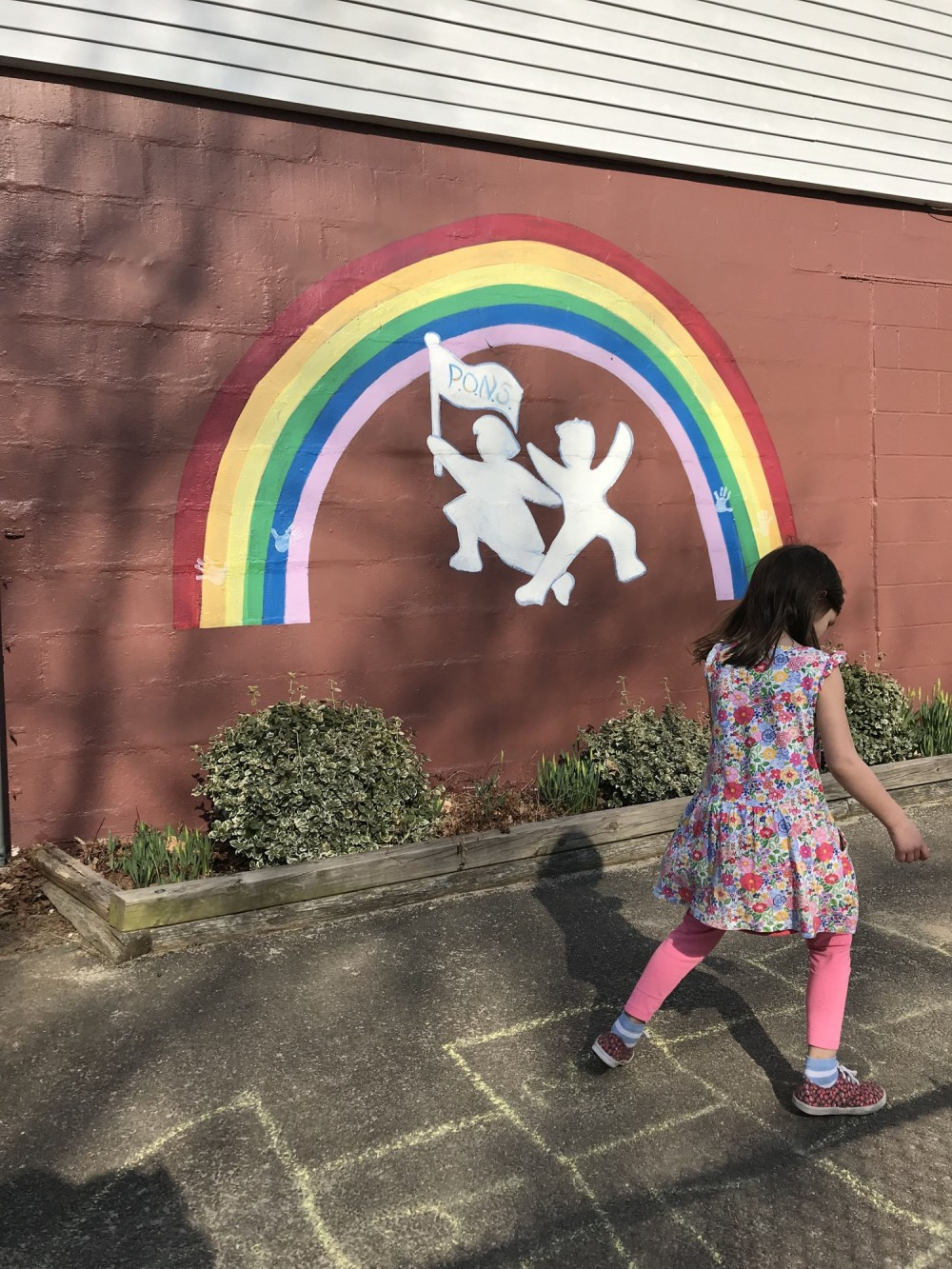 Child playing hopscotch in front of a mural of the Pine Orchard Nursery School logo.